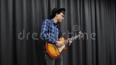 他用电吉他演奏。 情感吉他独奏。 年轻的职业音乐家吉他手，黑色时尚帽子演奏